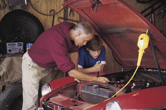 Photo of an adult showing an adolescent how to work on a car engine.