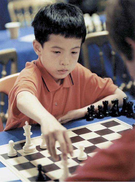 Photo of an eight-year-old chess prodigy playing a game of chess and reaching out to move a piece.