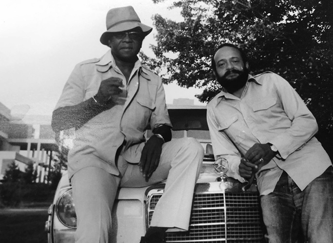 The photograph shows Austin Clarke and Andrew Salkey leaning against a Mercedes-Benz, posing casually.