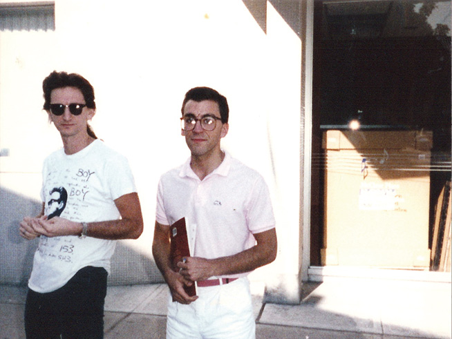 Geddy, in a white T-shirt and sunglasses, poses for a picture with Ray Wawrzyniak, a middle-aged man wearing glasses.