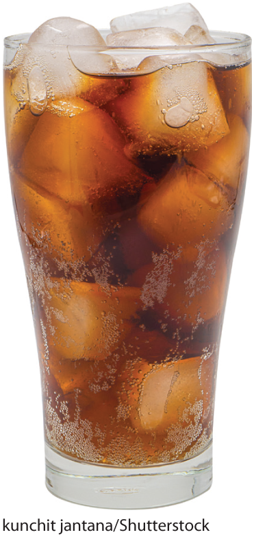 A photo shows a glass filled with a soft drink and ice cubes.