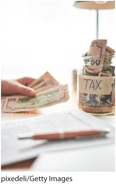 A photo shows money stuffed into a jar which is labeled, TAX. The backdrop shows a zoomed in view of a person’s hand holding money.