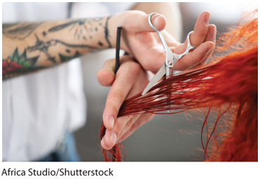 A photo shows a hair stylist trimming a person’s hair. 