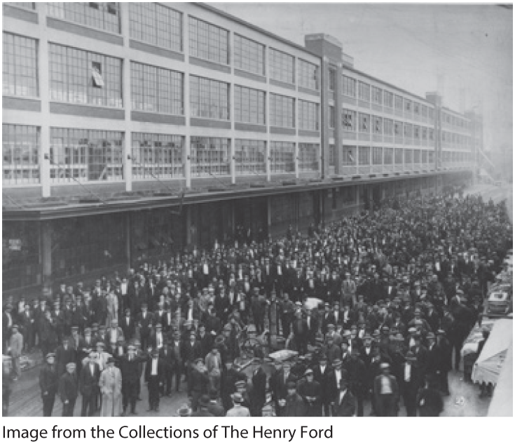 A photo shows a sea of people standing in front of the Ford plant.