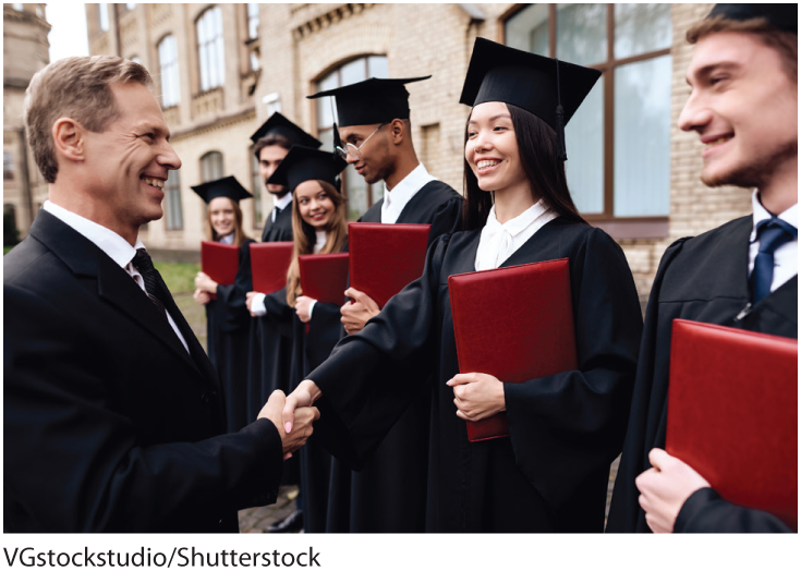 A photo shows a man in suit congratulating students in academic dress and holding a diploma. 