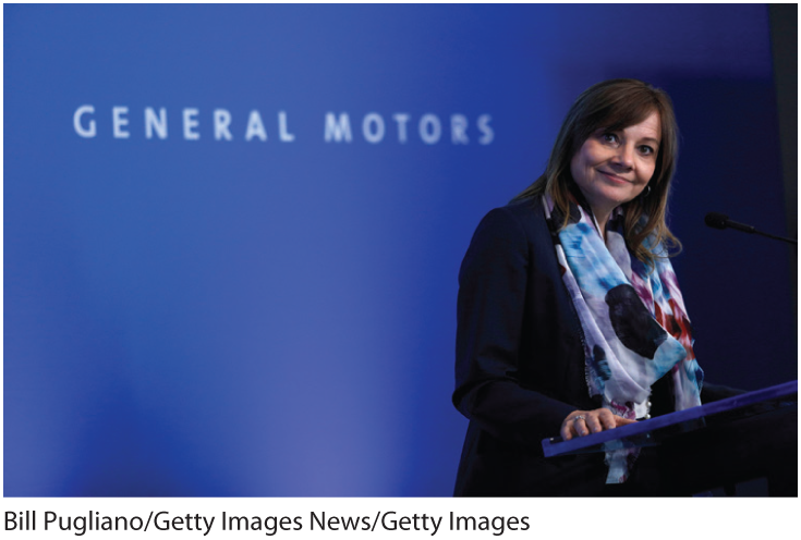 A photo shows Mary Barra standing at a podium with the logo of General Motors in the background. 