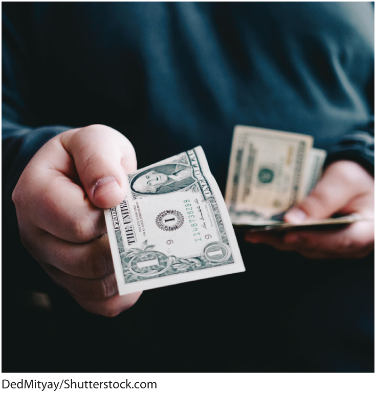 A photo shows a person holding US currency in one hand and holding out a Dollar bill with the right hand.