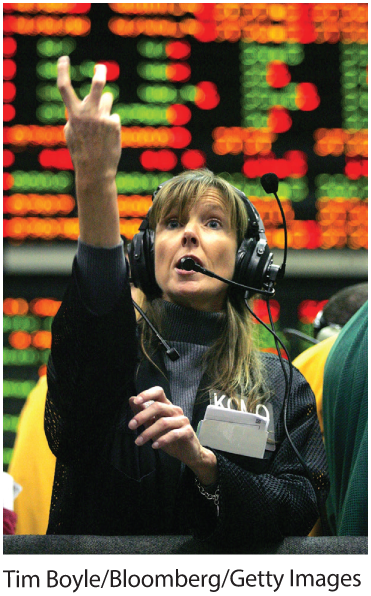 A photo shows a woman speaking over headphones in a stock market as she signals with one of the hands.