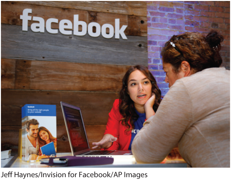 A photo shows two women talking in front of a laptop at Facebook’s headquarters.