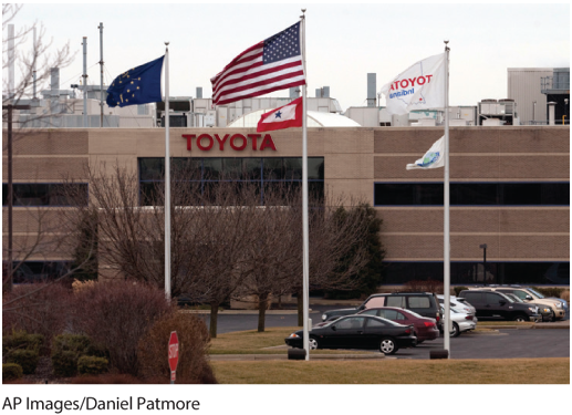 A photo shows the Toyota office front with flags of the European Union, the United States and Japan, by the parking lot.