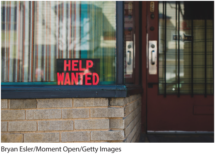 A photo shows a signboard on the window outside a building that reads, Help wanted. 