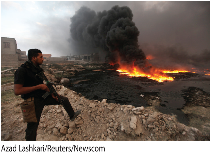 A photo shows thick dark smoke bellowing from a fire and a gunman watching from an elevated land in the foreground.