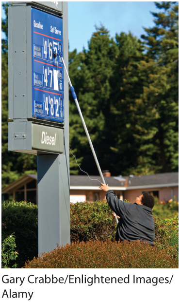 A photo shows a worker setting gas prices on a sign using a pole. 