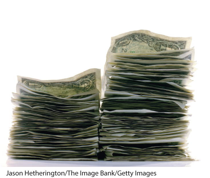 A photo shows two stacks of dollar bills. One stack is bigger than the other.