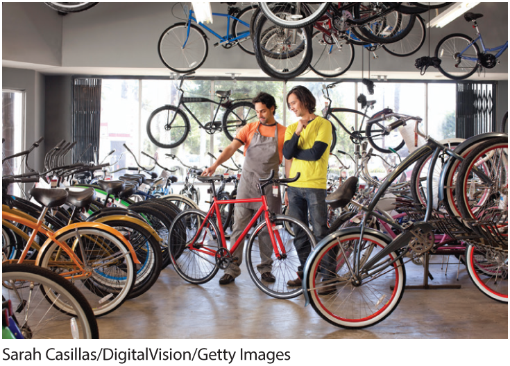 A photo shows two young men looking at bicycles in a bicycle shop. 