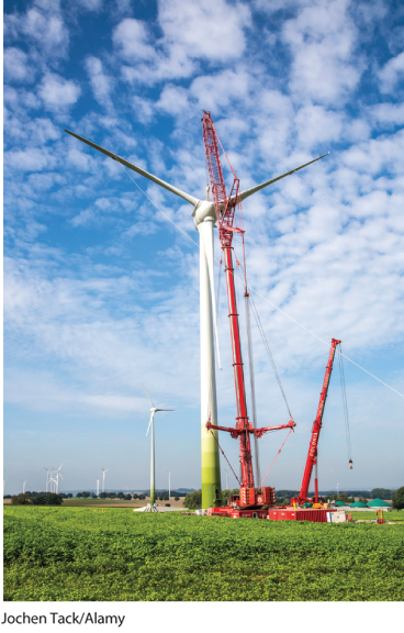 A photo shows a tower crane setting up a wind turbine.