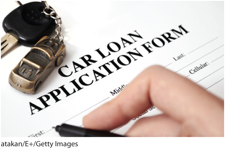 A photo shows a hand holding a pen over a car loan application form and a key with a car-shaped key ring on it. 