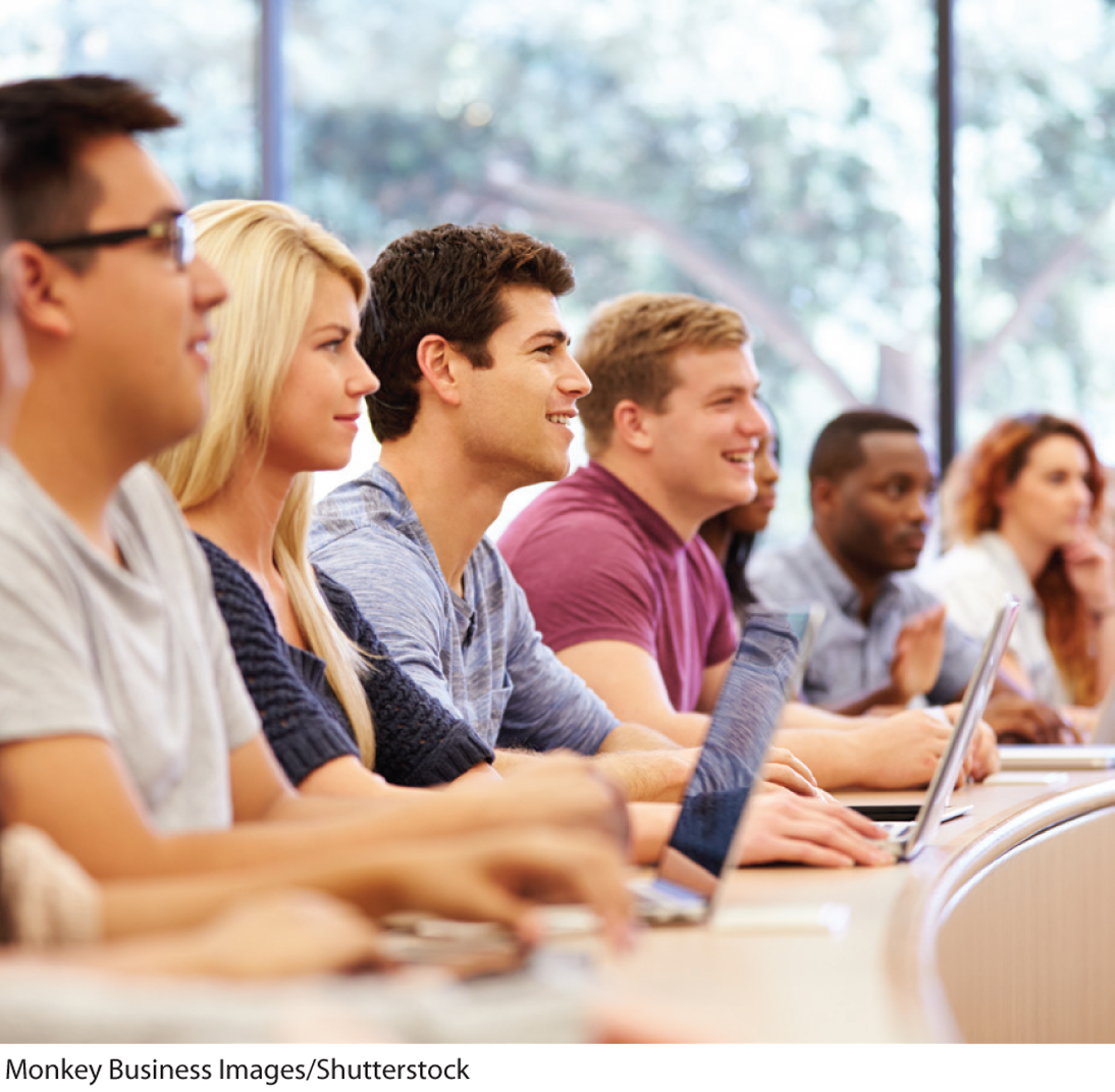 A photo shows young men and women sitting at a desk with laptops in a lecture hall.