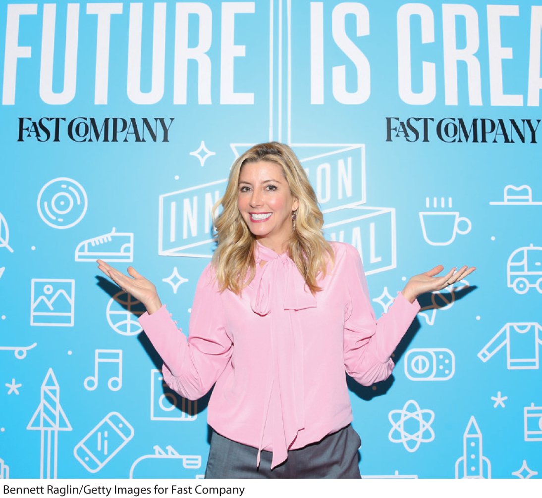 A photo shows Sara Blakely posing in front of a screen that reads, Fast Company. 