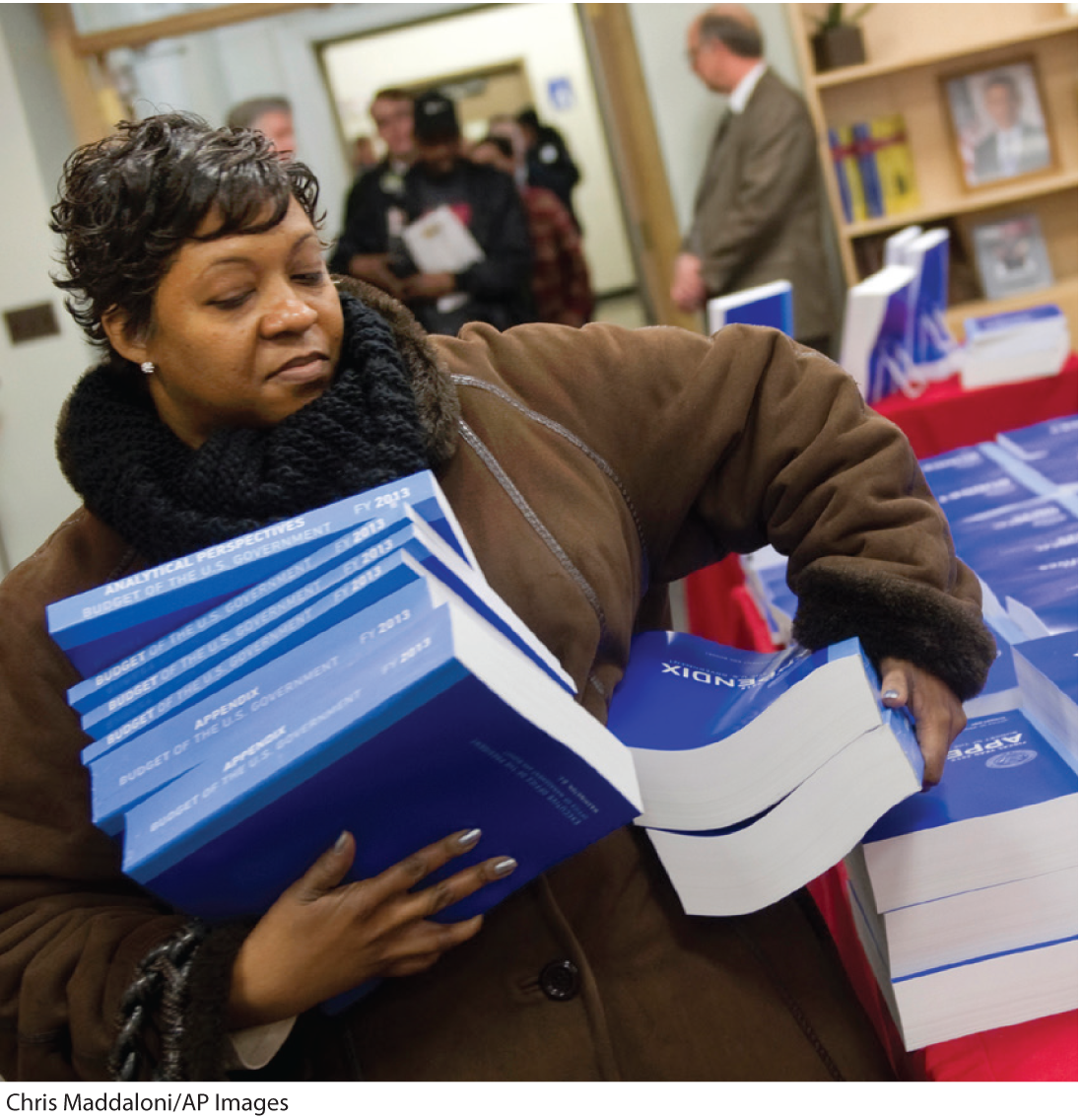 A photo shows a woman carrying a stack of multivolume books of the US Federal budget.