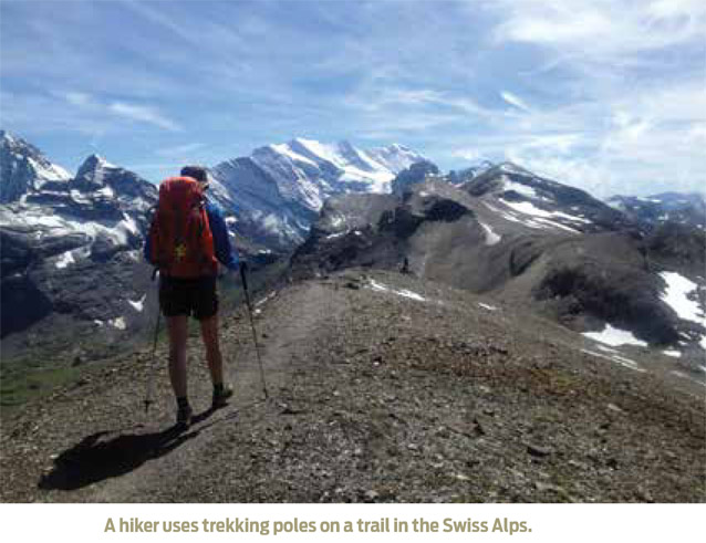 A hiker uses trekking poles on a trail in the Swiss Alps.