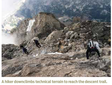 A hiker downclimbs technical terrain to reach the descent trail.