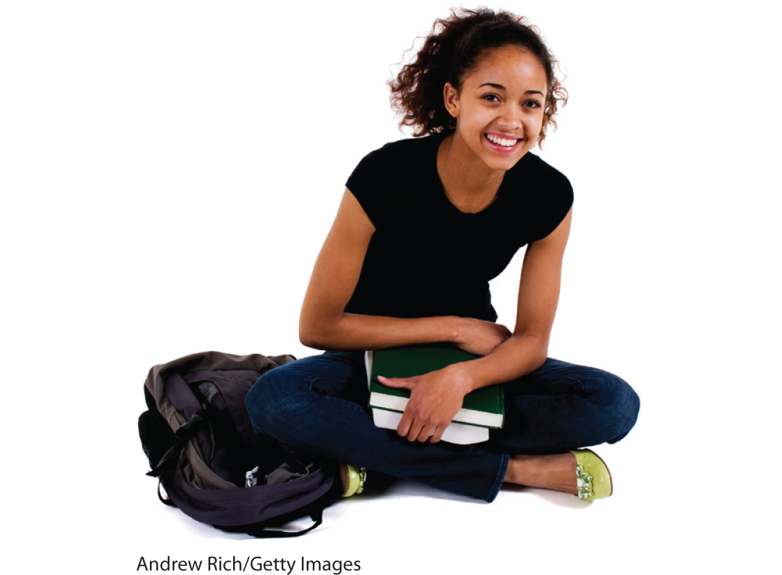 A photo shows a young woman sitting with her legs crossed and a bag beside her. She holds two books on her lap and smiles to pose.